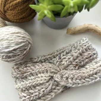 Handmade crochet headband in cream cotton next to balls of yarn