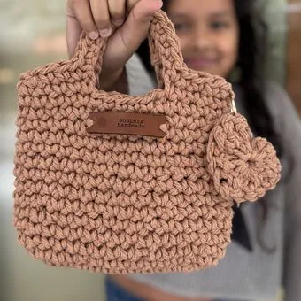 Child holding a small handmade crochet bag in dusty pink